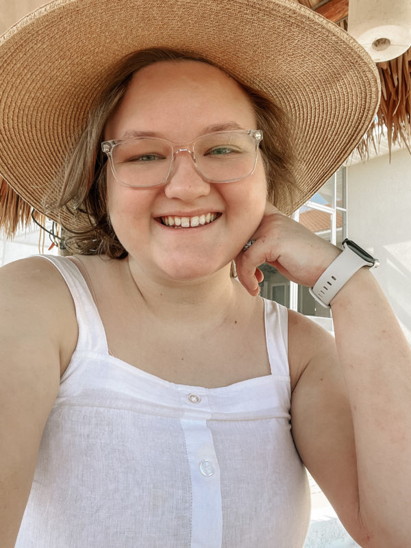 Elliot, a nonbinary person, takes a selfie in a white tank top and tan sun hat